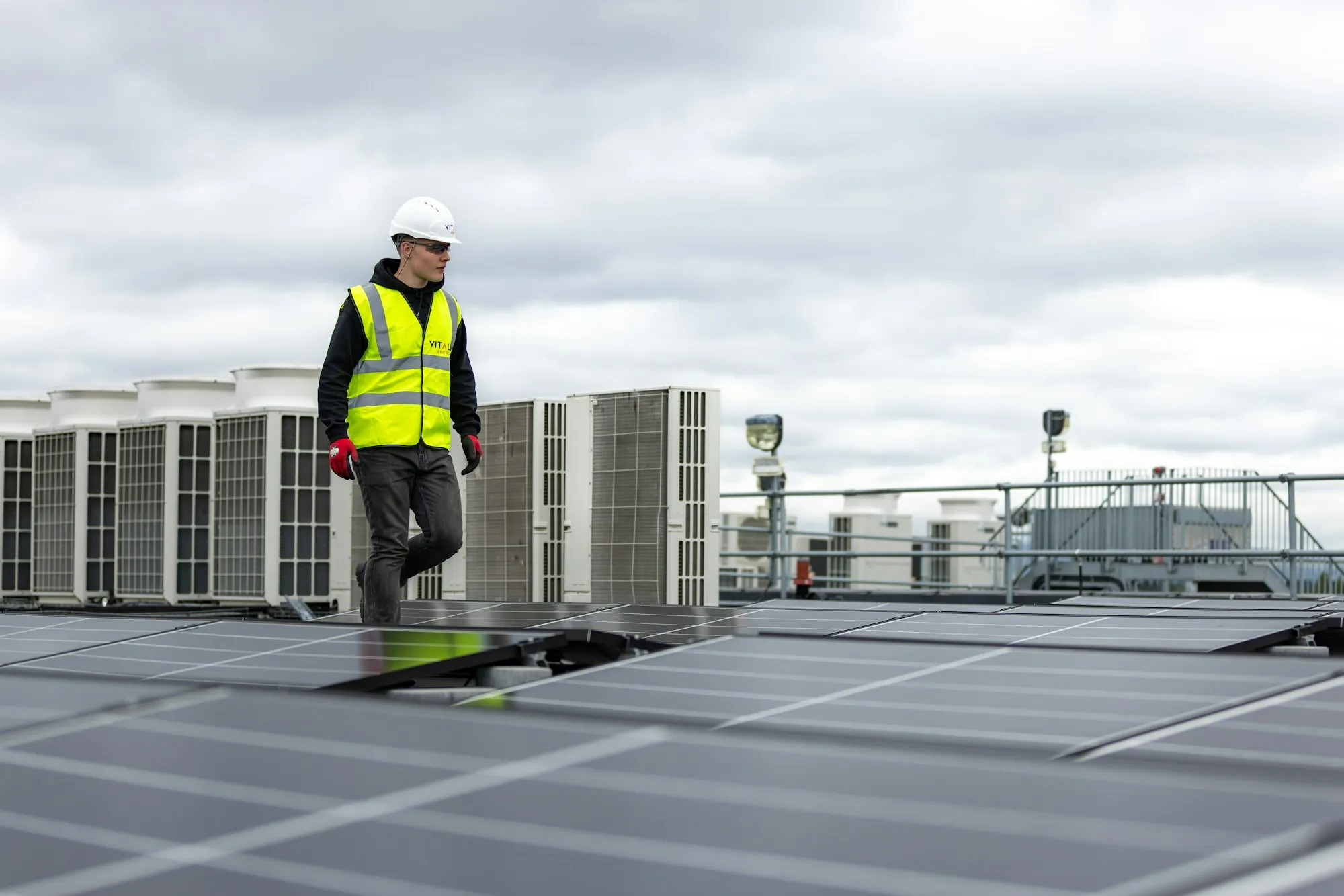 Worker walking on a rooftop past rows of HVAC units